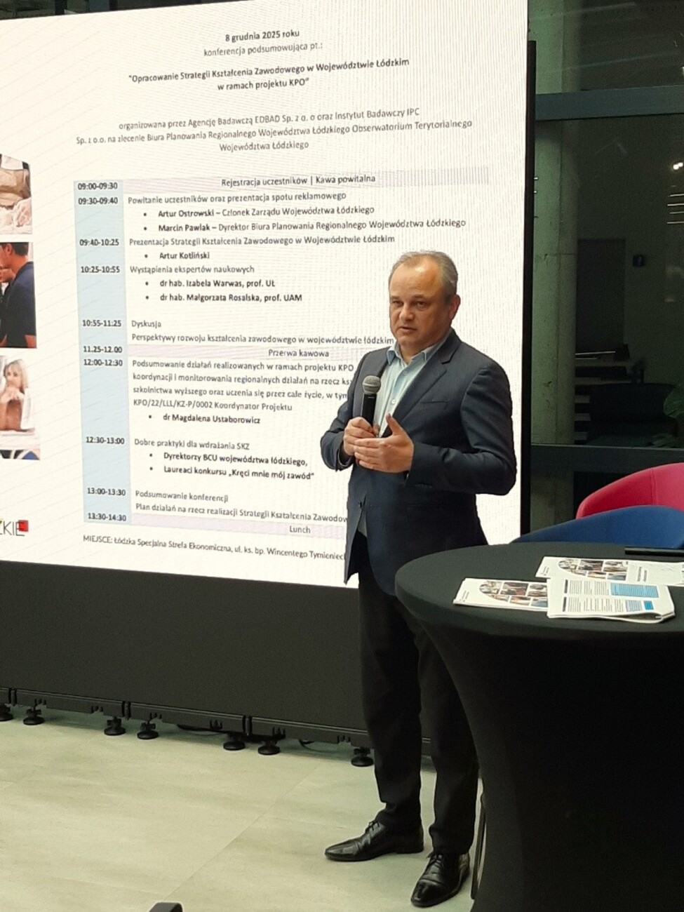 Zdjęcie przedstawia członka Zarządu Województwa Łódzkiego Pana Arura Ostrowskiego na tle ekranu, na którym jest wyświetlona agenda konferencji